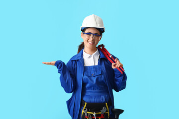 Asian female plumber with tool showing something on blue background