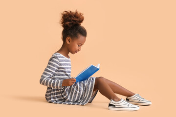 Little African-American girl reading book on beige background