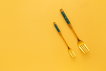 Stylish stainless steel forks on yellow background