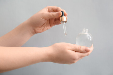 Woman applying serum onto her hand on light background, closeup