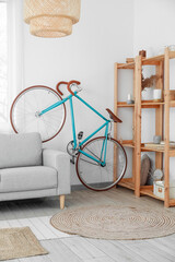 Interior of light living room with bicycle, grey sofa and wooden shelving unit