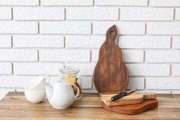 Cutting boards, jar with cookies and different utensils on kitchen counter near white brick wall