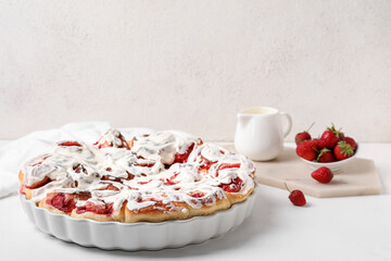 Baking dish with strawberry cinnamon rolls and cream on table against light wall