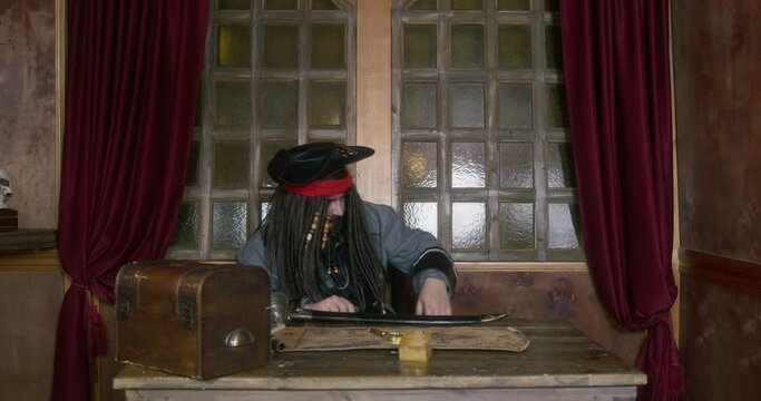 Portrait of pirate in cocked hat and wig with dreadlocks decorated with beads, who takes out small key, examines it and is going to open secret drawer or treasure chest with it, close up