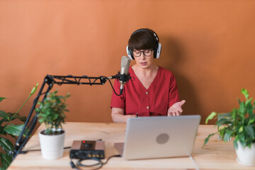 Middle-aged female radio presenter talking into the microphone and reading news - radio broadcast online concept - obrazy, fototapety, plakaty