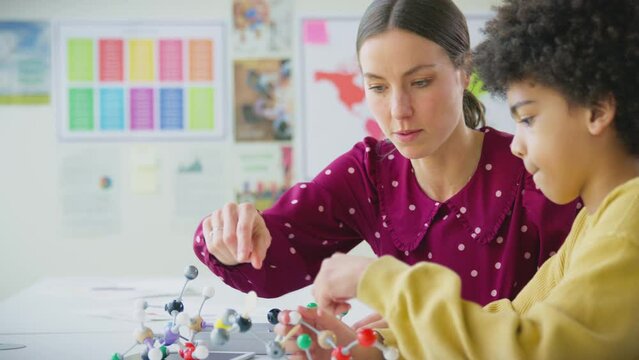 Male student with female teacher in classroom studying molecular model in science class - shot in slow motion