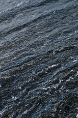 Black volcanic magnetic sand on the seashore. Background texture of the beach with waves closeup. 
