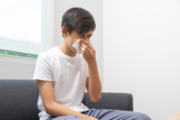 Sick Asian preteen boy blowing nose and sneeze at home, healthcare concept.