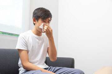 Sick Asian preteen boy blowing nose and sneeze at home, healthcare concept.