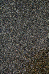 Black volcanic magnetic sand on the seashore. Background texture of the beach with waves closeup. 

