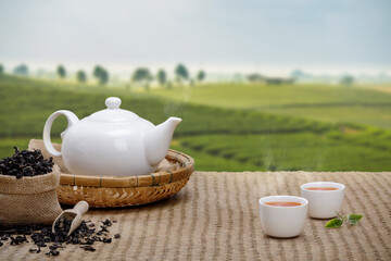 Warm cup of tea with teapot, green tea leaves and dried herbs on the bamboo mat at morning in plantations background with empty space, Organic product from the nature for healthy with traditional