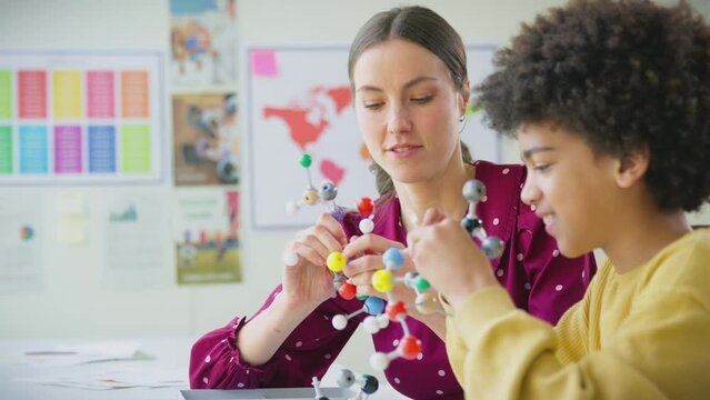 Male student with female teacher in classroom studying molecular model in science class - shot in slow motion