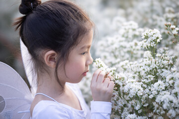 Cute little girl smelling flowers and wear a magic ballet fairy costume in beautiful white of...