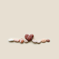 Aesthetic minimal flat lay sea pebble stones with heart, beige background. Composition from natural colored stone as wave. Balance, harmony, loving sea concept, top view card