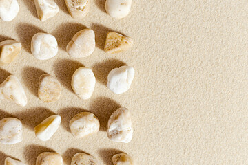 Fototapeta na wymiar Aesthetic minimal pattern with pebble stones on fine sand background. Top view on natural stone neutral yellow beige pastel colored image