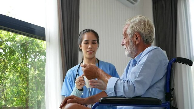 A caring Asian nurse gives a glass of water to an elderly male patient at the hospital. A friendly female doctor treats and gives medicine to an elderly male patient at a nursing home.
