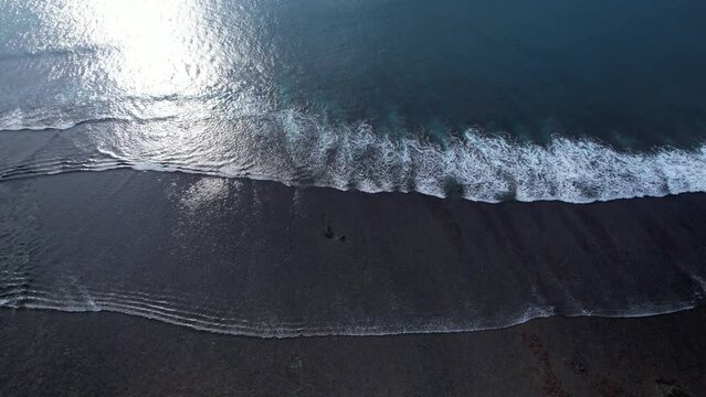 High angle aerial shot of waves and landswell at shallow place, ocean shore in low tide. Bali coastline at South Kuta, waves run towards shore and turn to whitewater, then water flow back
