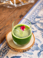 Healthy green smoothie in a clear glass garnished with rose petals. A  cup of healthy drinks made from kale and fruit juice, selective focus.