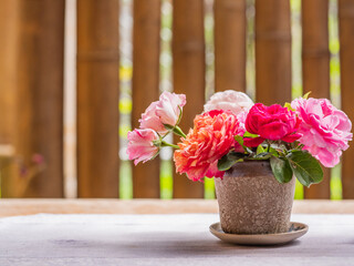 Beautiful pot of red and pink roses on the table against the bamboo wall, selective focus.