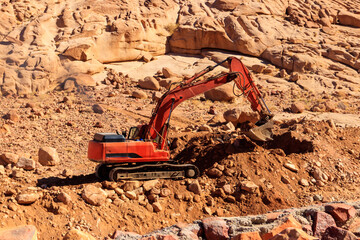 Orange excavator working at construction site in desert in Sinai peninsula, Egypt