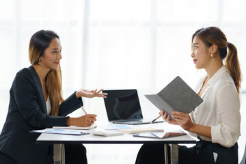 Two young Asian professional businesswomen working talking in a modern startup.