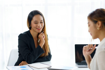Fototapeta premium Two young Asian professional businesswomen working talking in a modern startup.