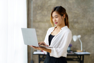 Successful young Asian businesswoman standing holding laptop in the office.
