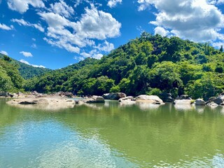 Tranquil natural scene with blue mountains, blue sky, and scattered rocks on the rippling river. Eco-tourism on a sunny day