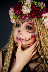 Naklejka premium Beautiful Halloween Make-Up Style. Blond curly hair Model Wear Sugar Skull Makeup with Red Roses. Santa Muerte concept. Model on black background in studio with wreath