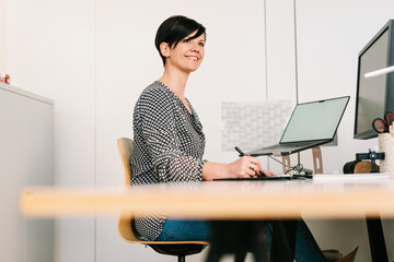 businesswoman sits in office in front of her computer and looks up laughing