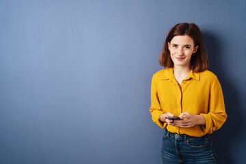 woman looking at camera with cell phone smiling, copyspace with blue background