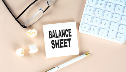 BALANCE SHEET text on sticky with pen ,calculator and glasses on beige background