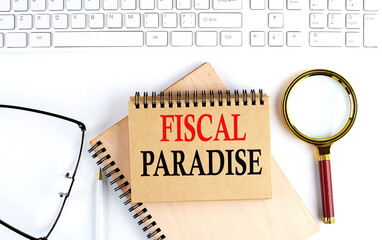 FISCAL PARADISE text in the office notebook with keyboard, magnifier and glasses , business concept
