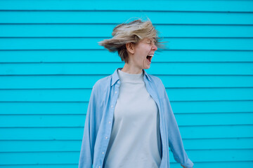 Portrait of middle-aged crazy woman with flying fair hair wearing grey T-shirt, blue shirt,...