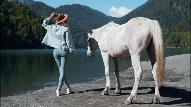 Mysterious woman tourist with animal horses wild white sunset running rider cowboy water Amazing view turquoise water high mountain lake Braies mountains. Casual boho style clothing back view