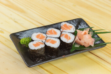 Sushi maki with salmon in a white plate placed on a wooden floor