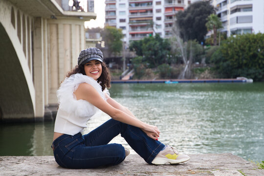 young, beautiful woman with dark, curly hair and an upturned nose is wearing a cap and sitting by a river. The woman is posing for photos. Concept expressions. smile, sad, thinking, enjoying, living.