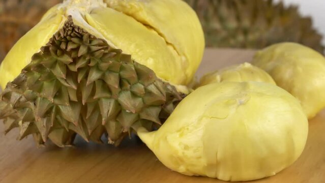 Closeup scene rotation of ripe peeled durian and pieces of peel on wooden board.