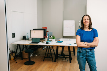 businesswoman stands with folded arms in office and looks into camera