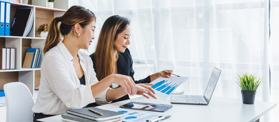 Beautiful Asian woman looks interested in online content on laptop in business office with her college friends.
