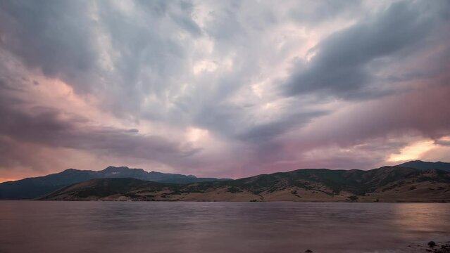 Sunset time-lapse over lake looking towards mountains as the landscape turns pink in color.
