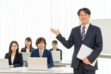 セミナーの男性講師とスーツ姿の男女（カメラ目線）
