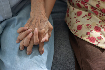 A close-up shot of a daughter and grandmother holding hands with warmth and encouragement.