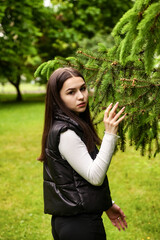 Portrait teenage girl walking in spring park in green fir trees or spruce