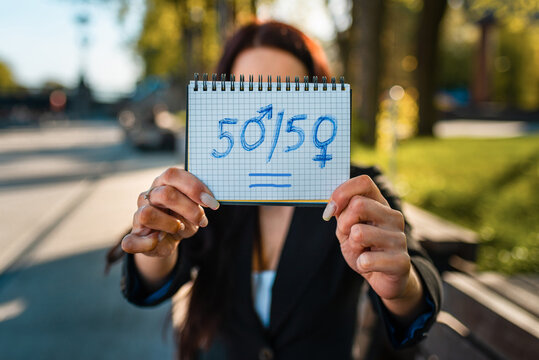 Beautiful young caucasian woman in the street park shows the text 50-50. with the zeros signs as the female and male gender symbols,sunset summer evening.Close-up.