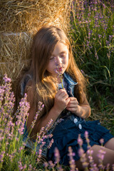 Cute little child girl in lavender field with in a straw hat sniffing fragrant lavender sprig