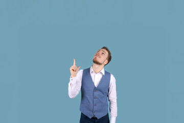 Young bearded business man standing near Copy space on blue wall background, isolated. Looking up,...