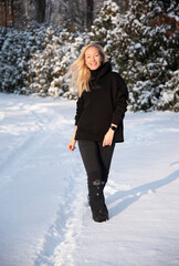  happy smiling beautiful blonde woman in black winteк cloth with hood walking in winter forest  