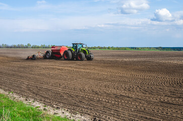 Obraz premium Tractor in the field, spring sowing. Sowing corn in the field in spring.