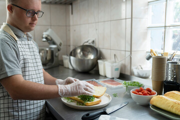 Caucasian man with down syndrome preparing a sandwich in commercial kitchen